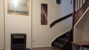 A spacious room with a wooden floor, a fireplace, a staircase, and a framed picture on the wall.