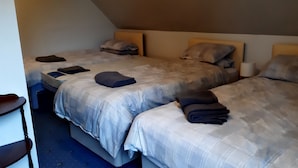 A hotel room with three beds, each with a headboard and pillows. There is a small table with a lamp and a folded blanket on one of the beds. - 1 Bed Flat - Sleeps 4 - Garden - Parking - Wifi (Inverness)