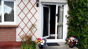 A house with a brick exterior, a white door with a glass panel, and a lattice fence. There are two flower pots with colorful flowers in front of the door. - 1 Bed Flat - Sleeps 4 - Garden - Parking - Wifi (Inverness)