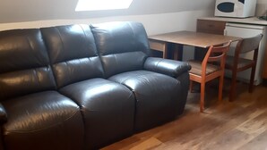A dark brown leather sofa in a room with a wooden table and two wooden chairs. - 1 Bed Flat - Sleeps 4 - Garden - Parking - Wifi (Inverness)