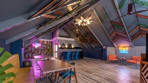 A modern loft-style room with a wooden floor, a dining table, and blue chairs. There is a neon sign that reads "Villa Monte You." - Villa Calangute Phase 11 (Calangute)