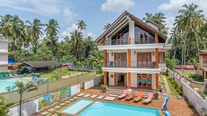 A two-story resort with a swimming pool, lounge chairs, and palm trees. - Villa Calangute Phase 11 (Calangute)