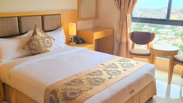 A hotel room with a large bed, a bedside table with a lamp, a chair, and a view of the city through the window.