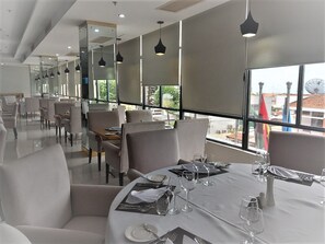 A restaurant with round tables set for dining, large windows with a view, and pendant lighting. - HOTEL EXPRESS (Luanda)