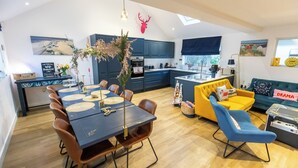 Een moderne keuken met donkerblauwe kastjes, een eethoek met een donkere tafel en bruine stoelen, een gele bank en een decoratie van een hertenkop op de muur.