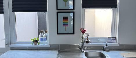 A modern kitchen with a built-in washing machine, a sink, and two windows with black blinds.