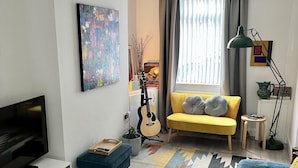 Una sala de estar moderna con televisor, guitarra, sofá y alfombra colorida.