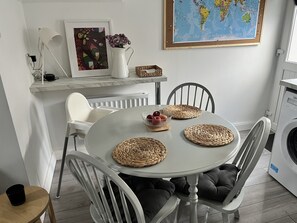 Uma sala de jantar com uma mesa redonda, jogos americanos trançados, uma tigela de frutas e um mapa-múndi na parede.