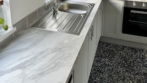 Una cocina moderna con encimera de mármol, pileta de acero inoxidable y muebles blancos.
