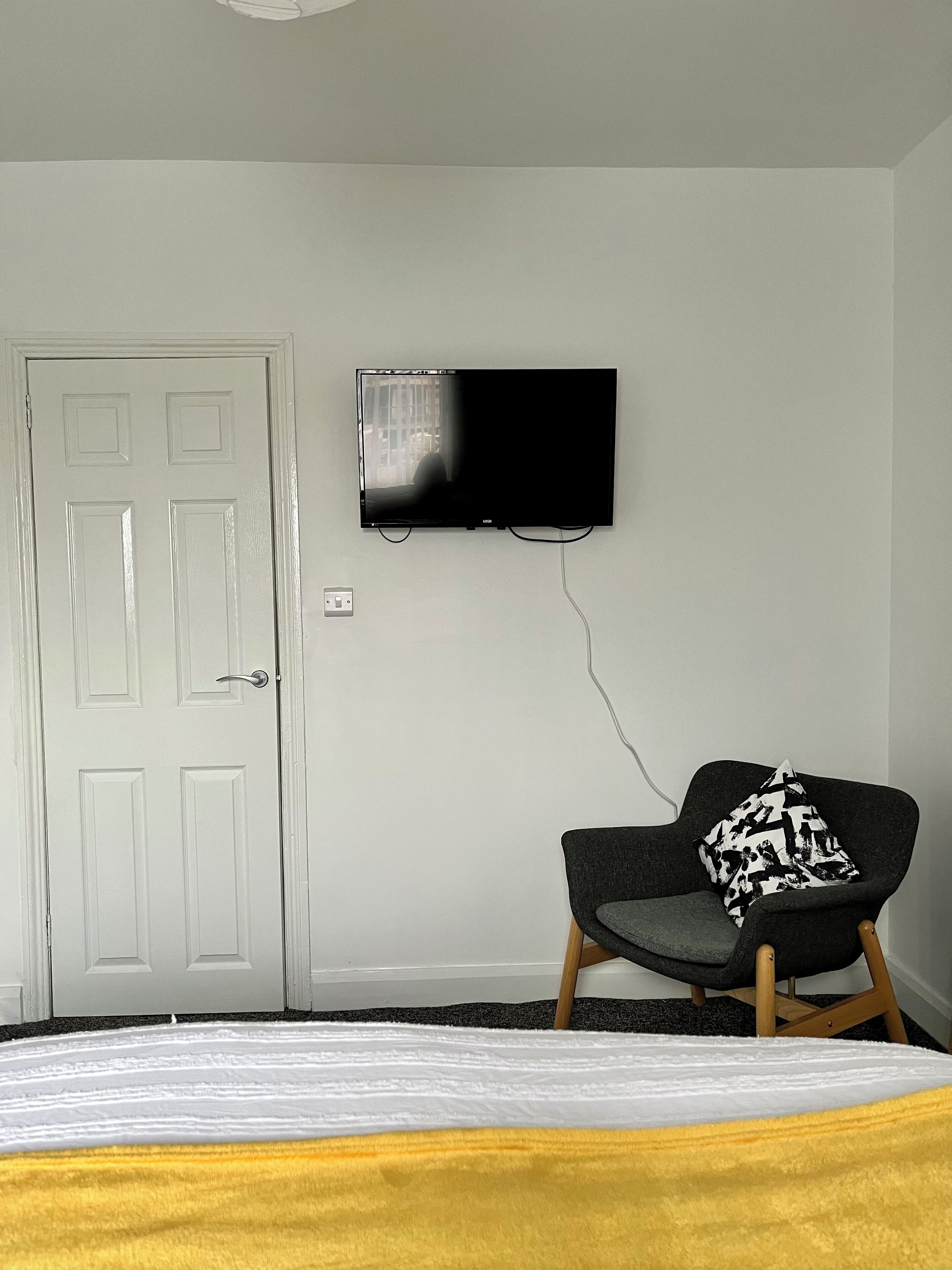 A bedroom with a bed, a chair, a television mounted on the wall, and a door.