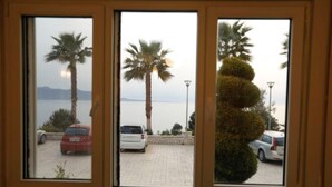 Vista a través de una ventana de tres paneles, mostrando un estacionamiento con coches, palmeras y una masa de agua al fondo.