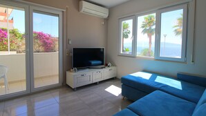 Una sala de estar con televisión, sofá y balcón con vista al mar.