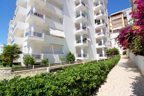 A multi-story residential building with balconies, a paved pathway, and lush greenery. - Albania Dream Beachfront Apartment  (Sarandë)