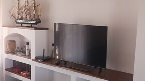 Een woonkamer met een televisie op een houten standaard, een scheepsmodel en een schilderij.