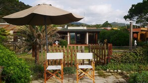 Een terras met twee houten stoelen onder een grote parasol, omgeven door weelderige begroeiing en een houten hek.