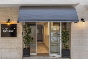 L’entrée d’un hôtel, avec un auvent sombre, des portes vitrées et des plantes en pot de chaque côté.