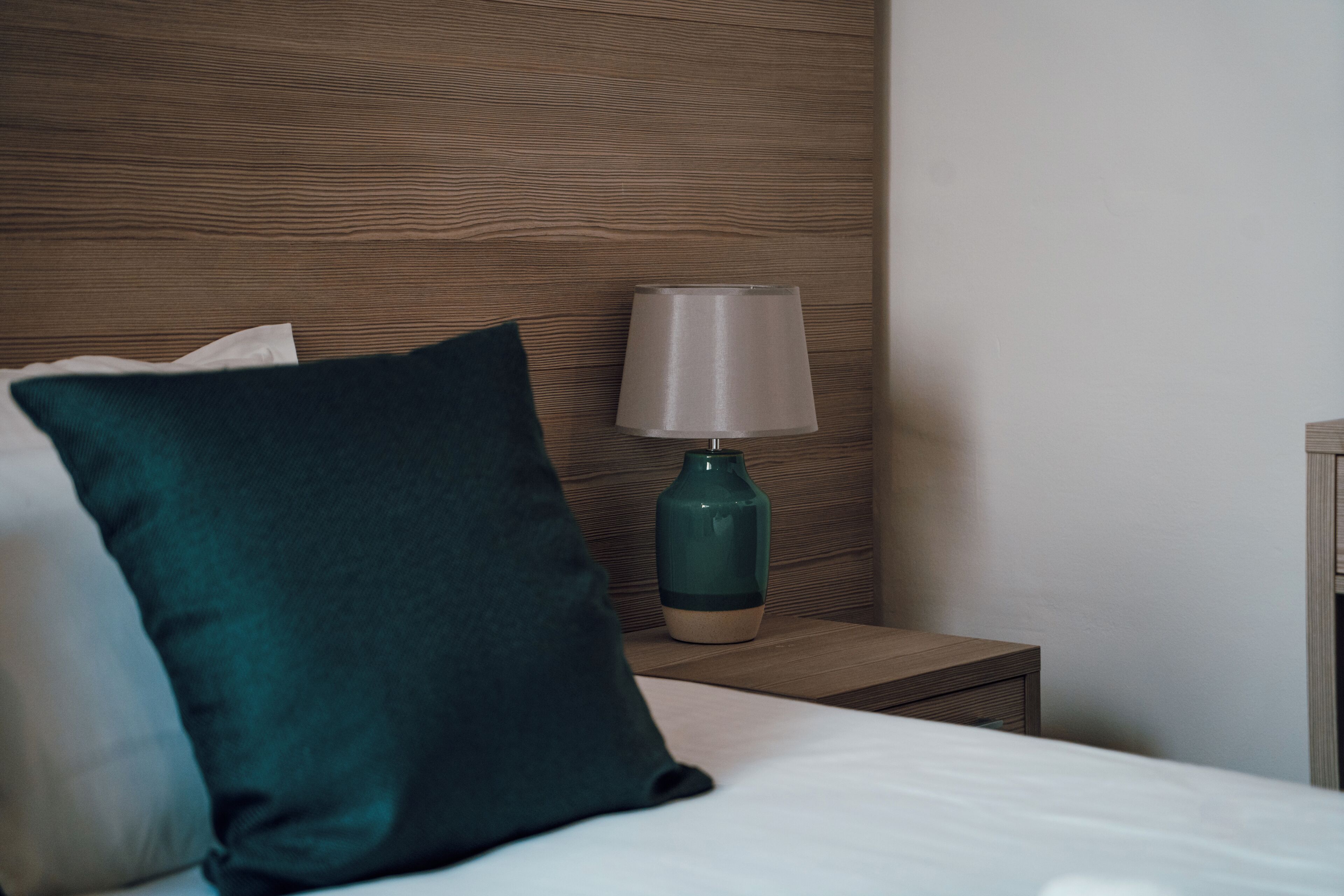 Un lit bien fait, agrémenté d’un oreiller turquoise, d’une lampe de chevet et d’une tête de lit en bois.