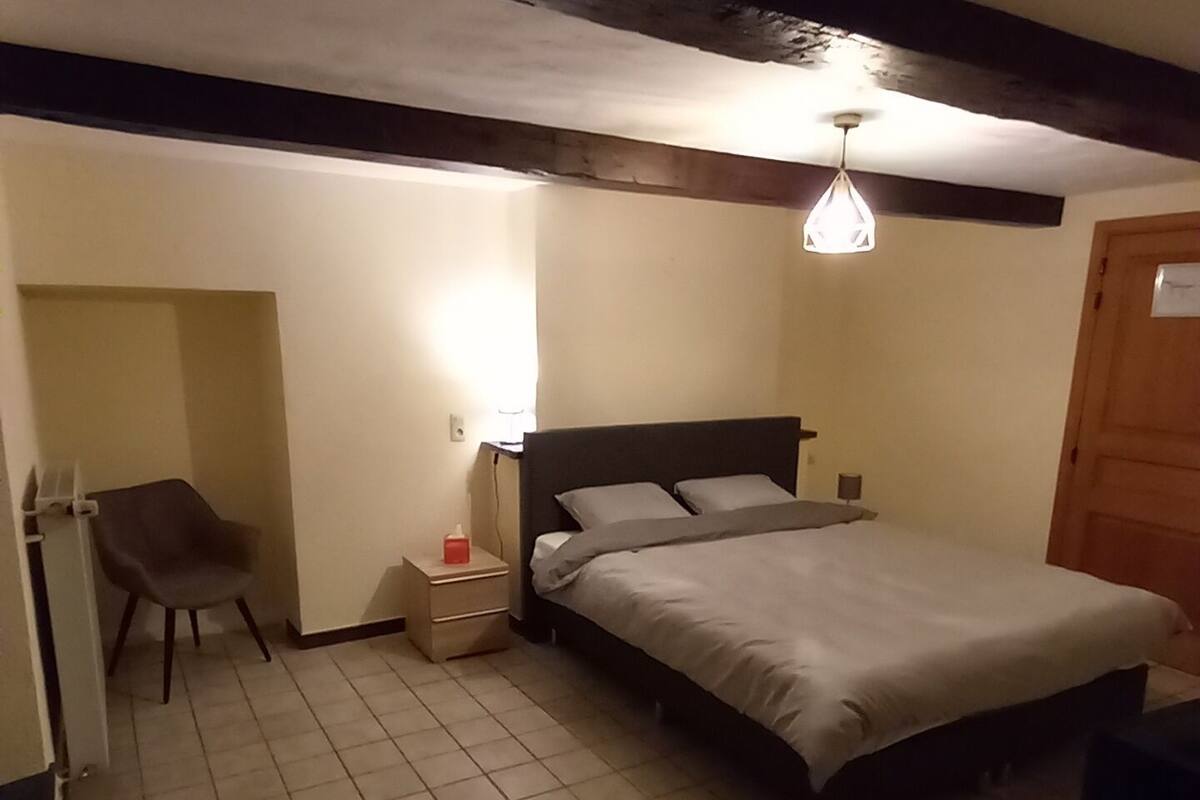 Ein Schlafzimmer mit Bett, Nachttisch, Stuhl und einer Pendelleuchte.