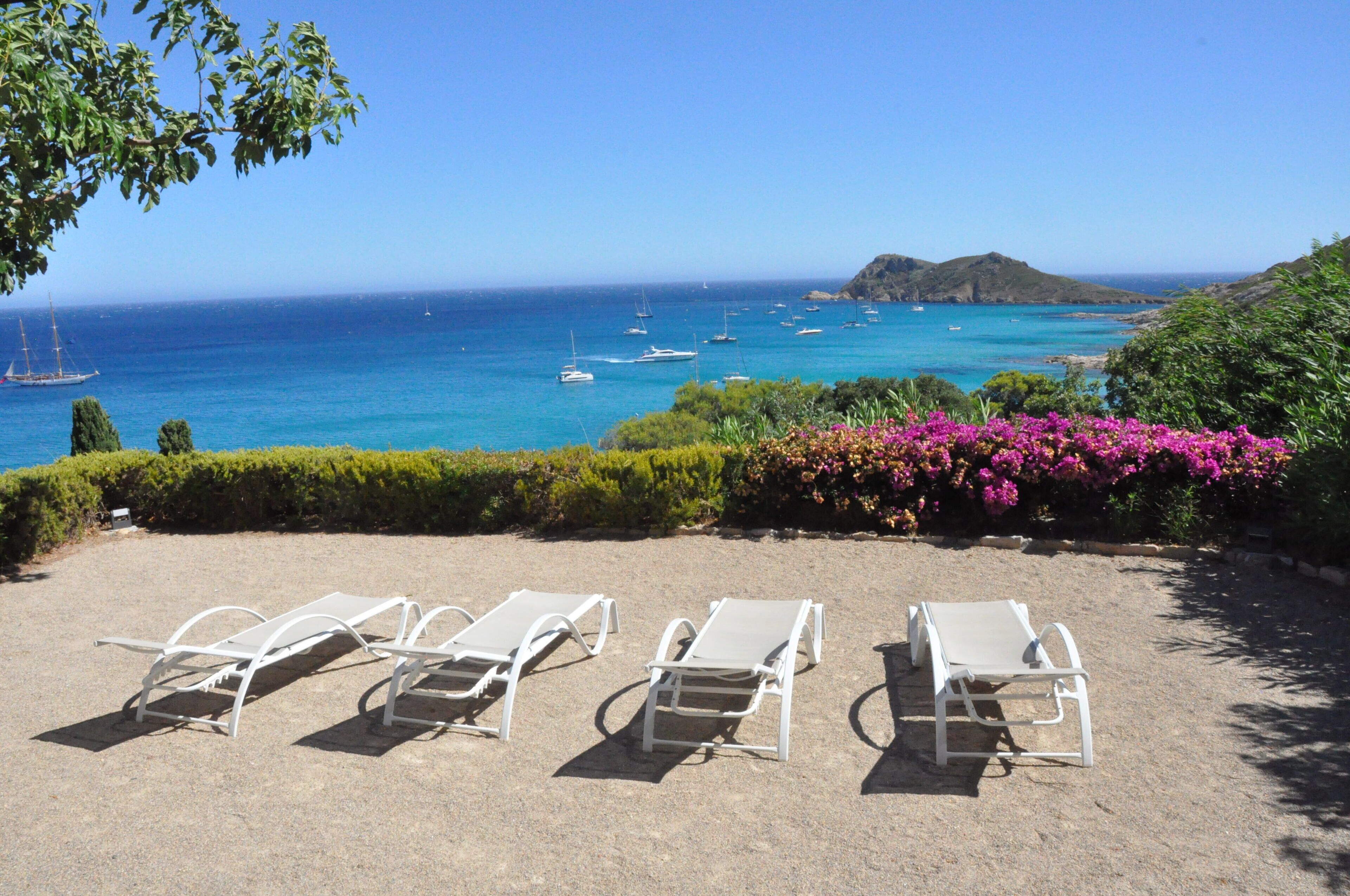 A beach with white lounge chairs and a view of the sea.