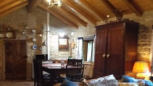 A rustic room with a stone wall, wooden ceiling beams, a sofa with patterned cushions, a dining table with chairs, and a wooden cabinet. - Romantic house in the woods - lafossa.eu
Breakfast included (Vetto)