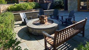 Un espace patio doté d’un foyer en pierre, de sièges d’extérieur et offrant une vue sur un bâtiment moderne.