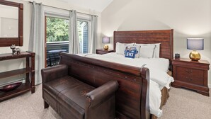 Une chambre à coucher avec un grand lit, un banc en bois, une commode et une table avec une lampe.