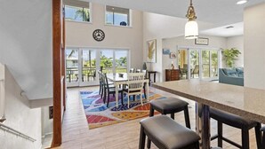 A spacious kitchen with a large island, a dining area with chairs and a table, and a view of the outdoors through large windows. - Sombrero Beach Beauty~ 50` Dock Private Pool Home! (Marathon)