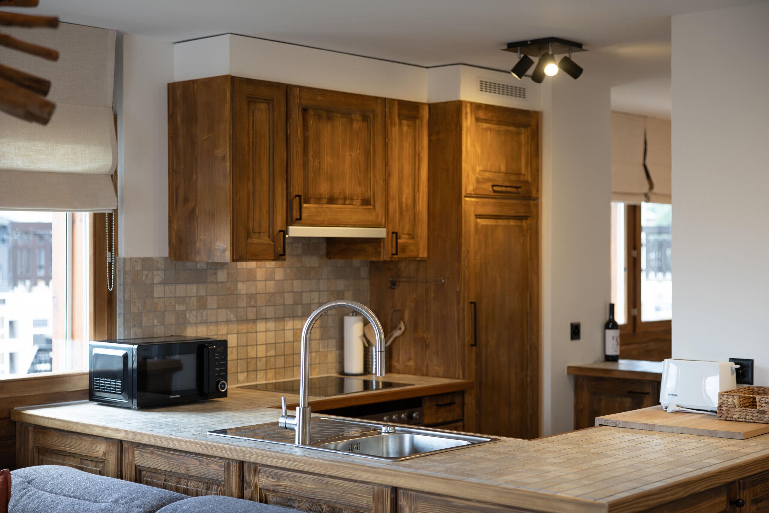 A kitchen with wooden cabinets, a stainless steel sink, a microwave, and a wine bottle.