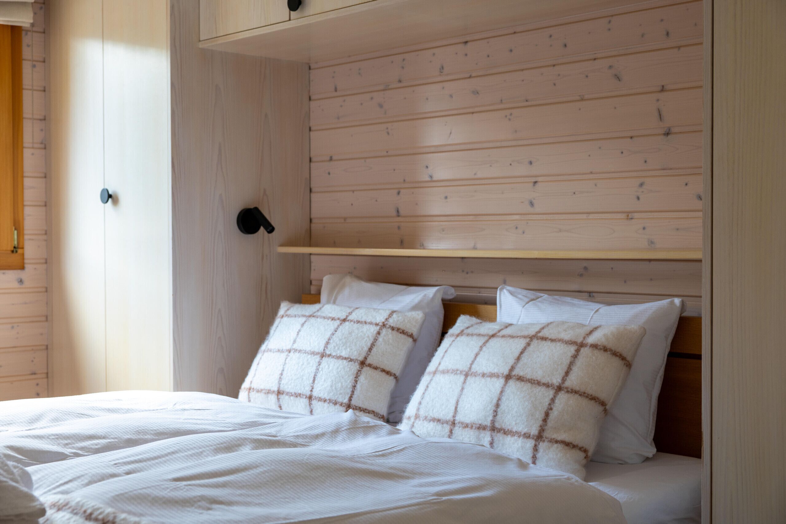 A bed with two pillows, a wooden headboard, and a white wall.