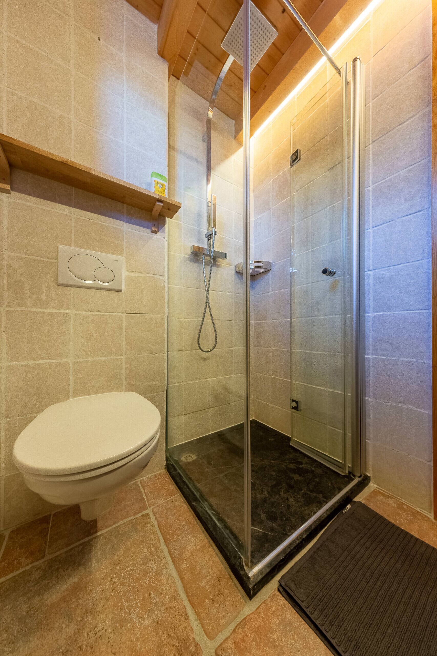 A modern bathroom with a glass-enclosed shower, a toilet, and a shelf above the toilet.
