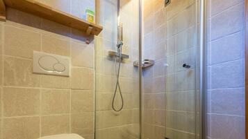 A modern bathroom with a glass-enclosed shower, a toilet, and a shelf above the toilet.