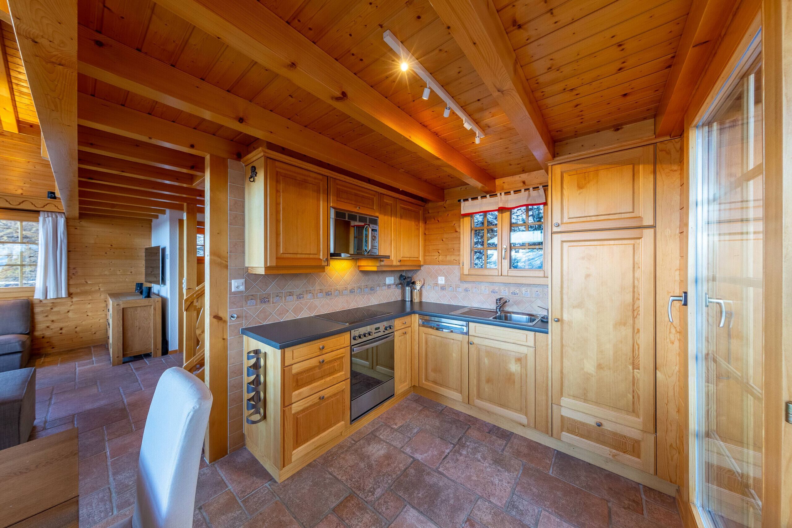 A wooden cabin interior with a kitchen area featuring wooden cabinets, a stove, and a sink.