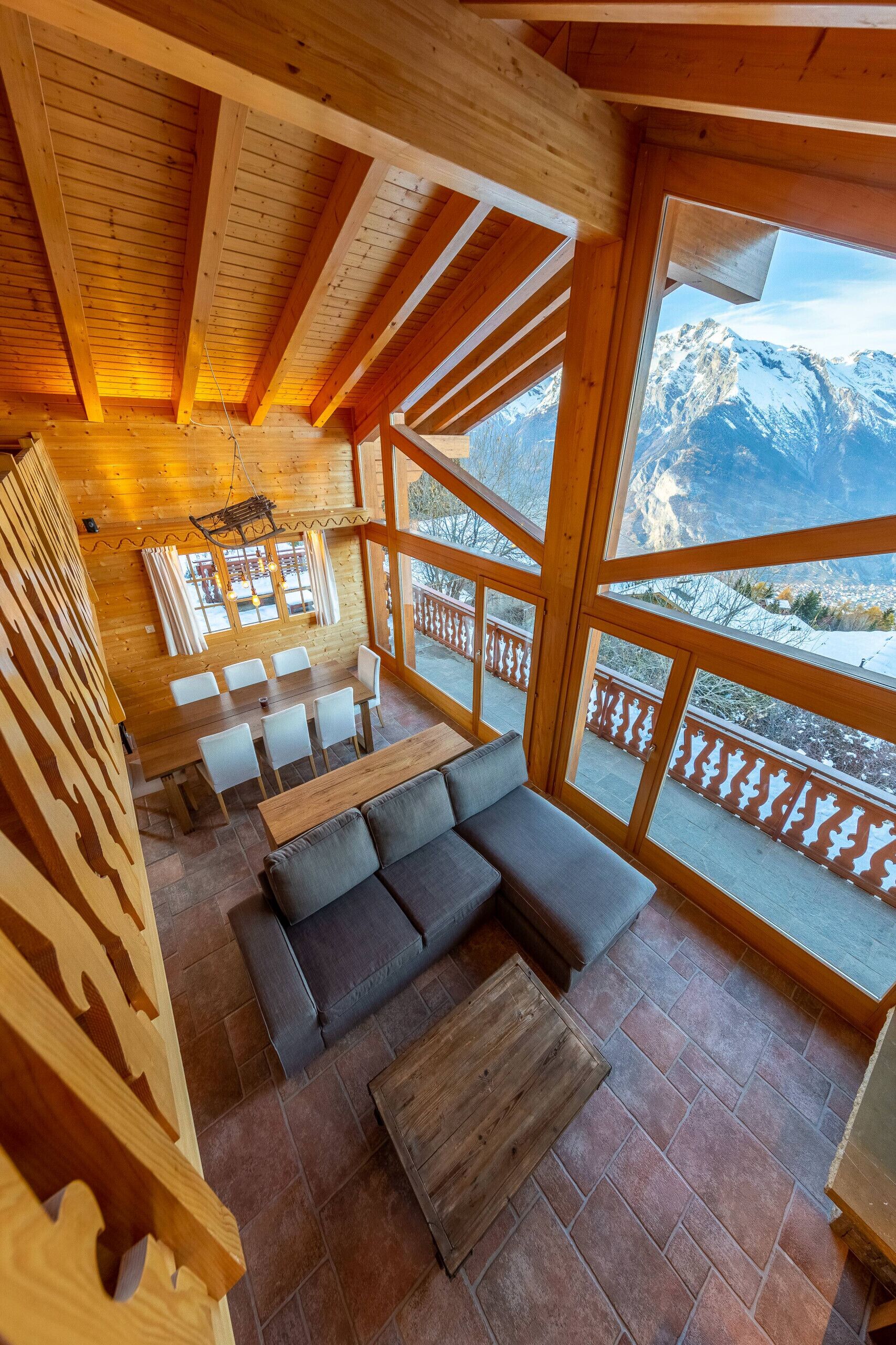 Un intérieur en bois comprenant un coin repas, un canapé et une vue sur des montagnes enneigées.