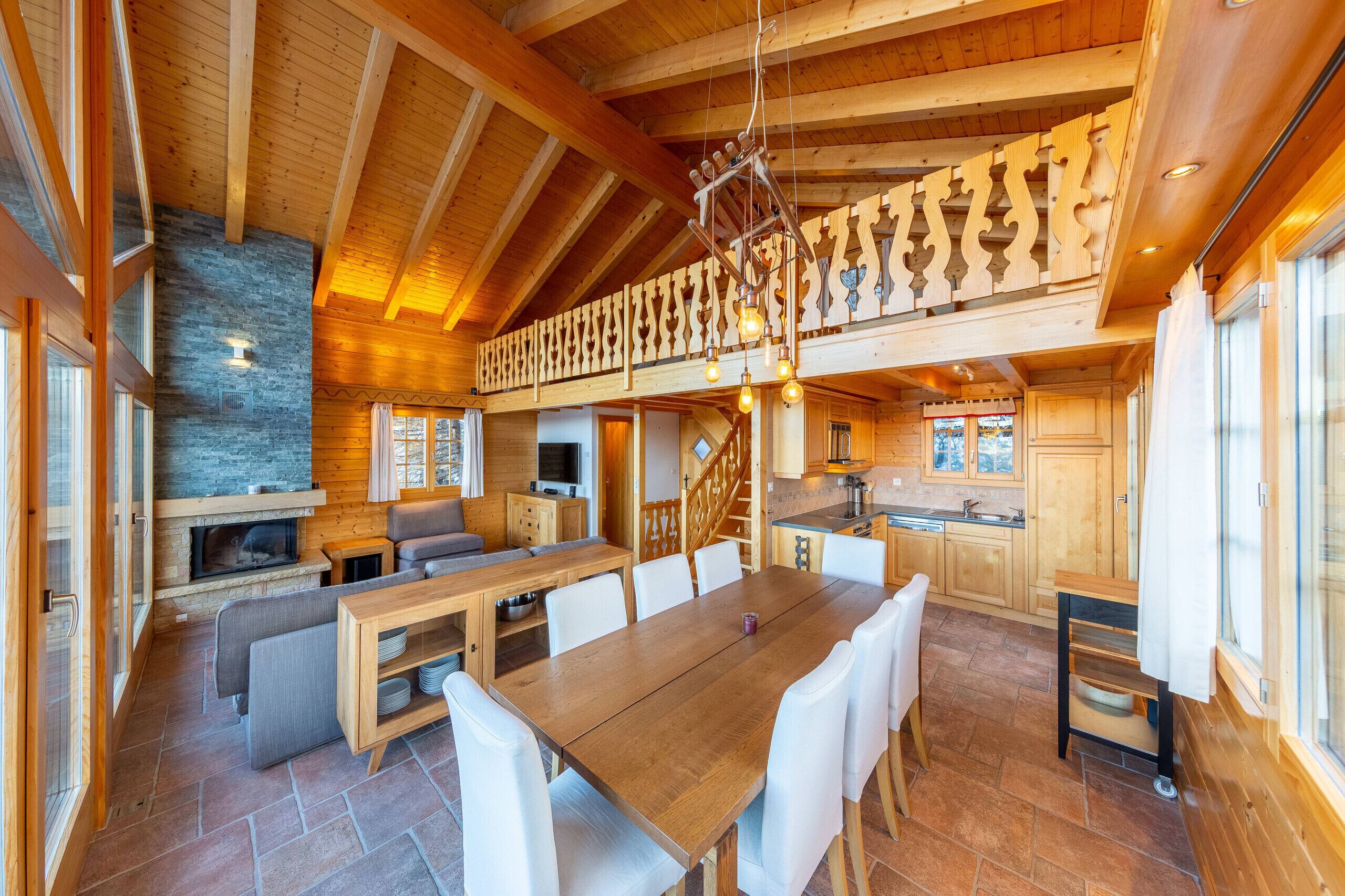 Un comedor amplio con una larga mesa de madera y sillas blancas, una chimenea y una pared de piedra.