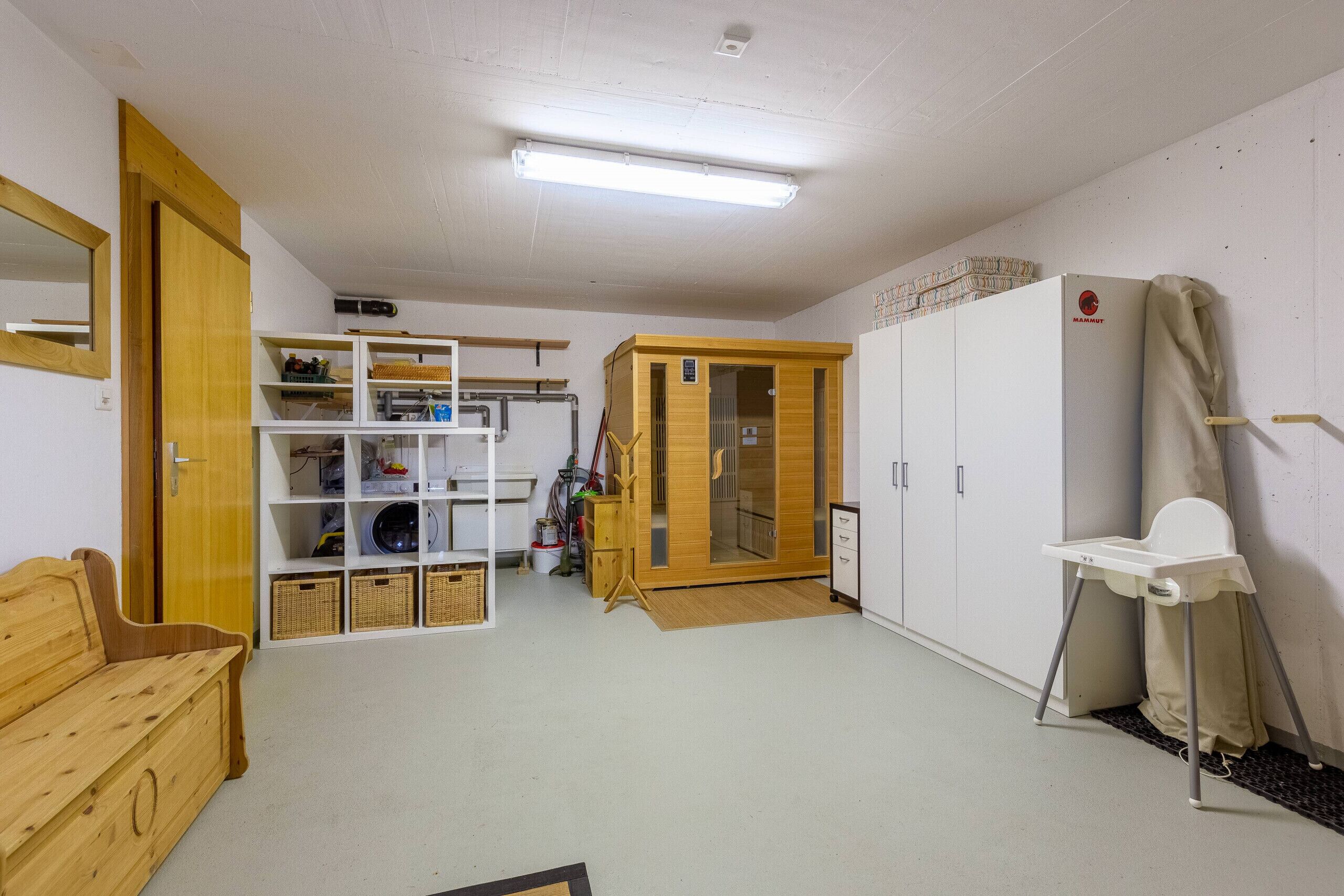 A room with a wooden bench, white shelves, a wardrobe, and a small white table with a chair.