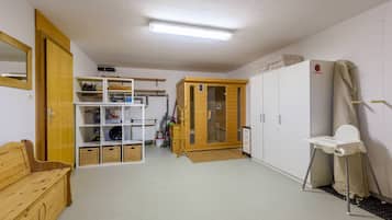 A room with a wooden bench, white shelves, a wardrobe, and a small white table with a chair.