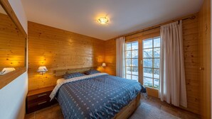 Ein Schlafzimmer mit Holzwänden, einem großen Bett, zwei Nachttischlampen und einem Fenster mit Vorhängen.