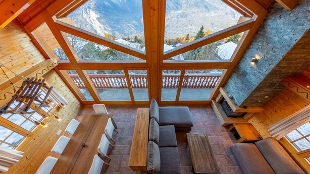 Ein Holzinnenraum mit hoher Decke, großen Fenstern und Blick auf Berge.