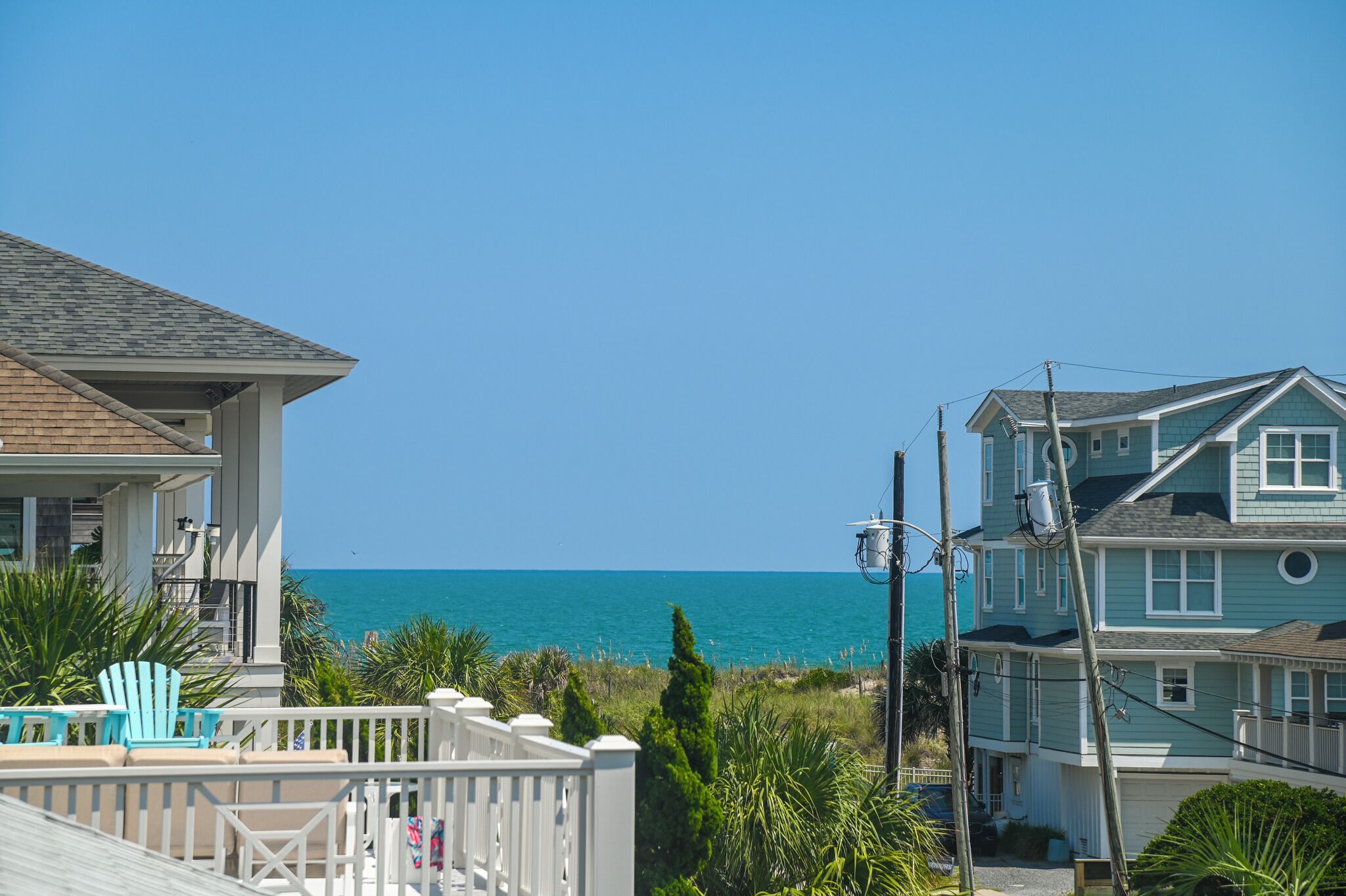 A coastal residential area with houses, a clear blue sky, and the ocean in the background.