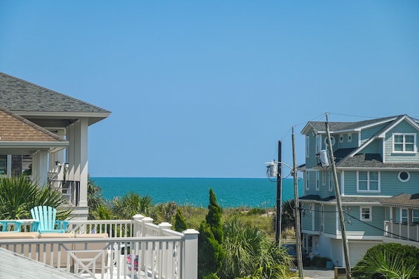 A coastal residential area with houses, a clear blue sky, and the ocean in the background.