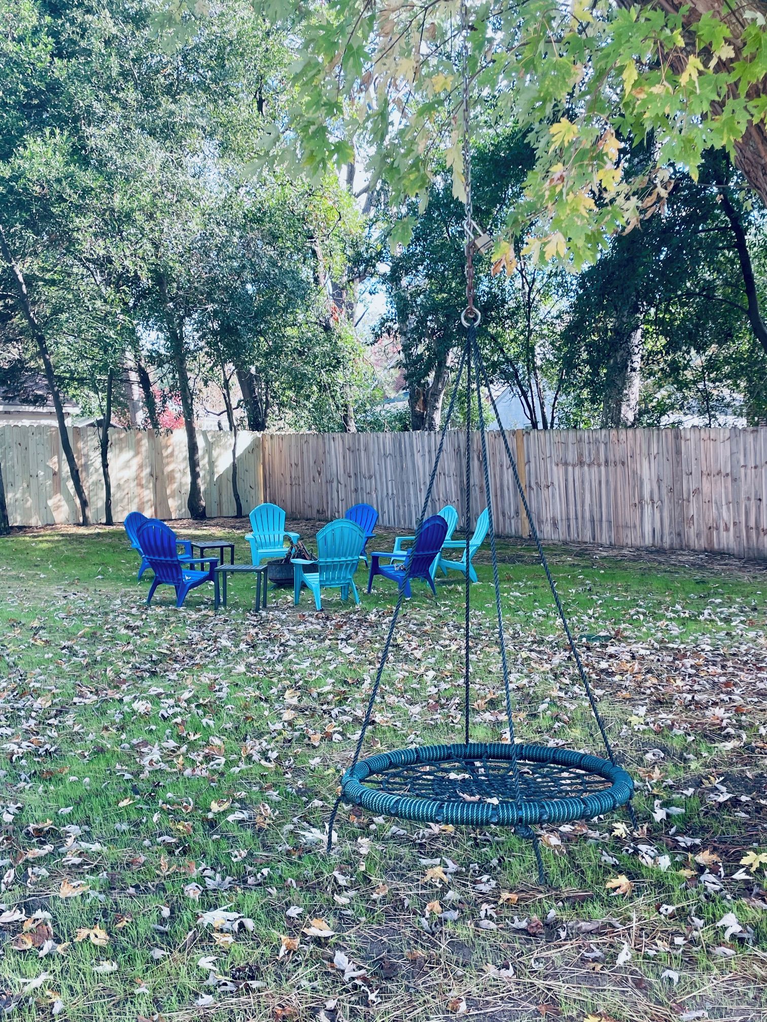 A backyard with a swing set, blue chairs, and a table.