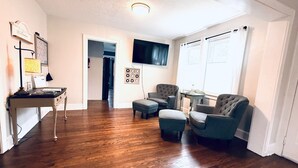 Un salon doté de parquets en bois, d’un téléviseur fixé au mur et d’un espace détente comprenant un canapé et des fauteuils.