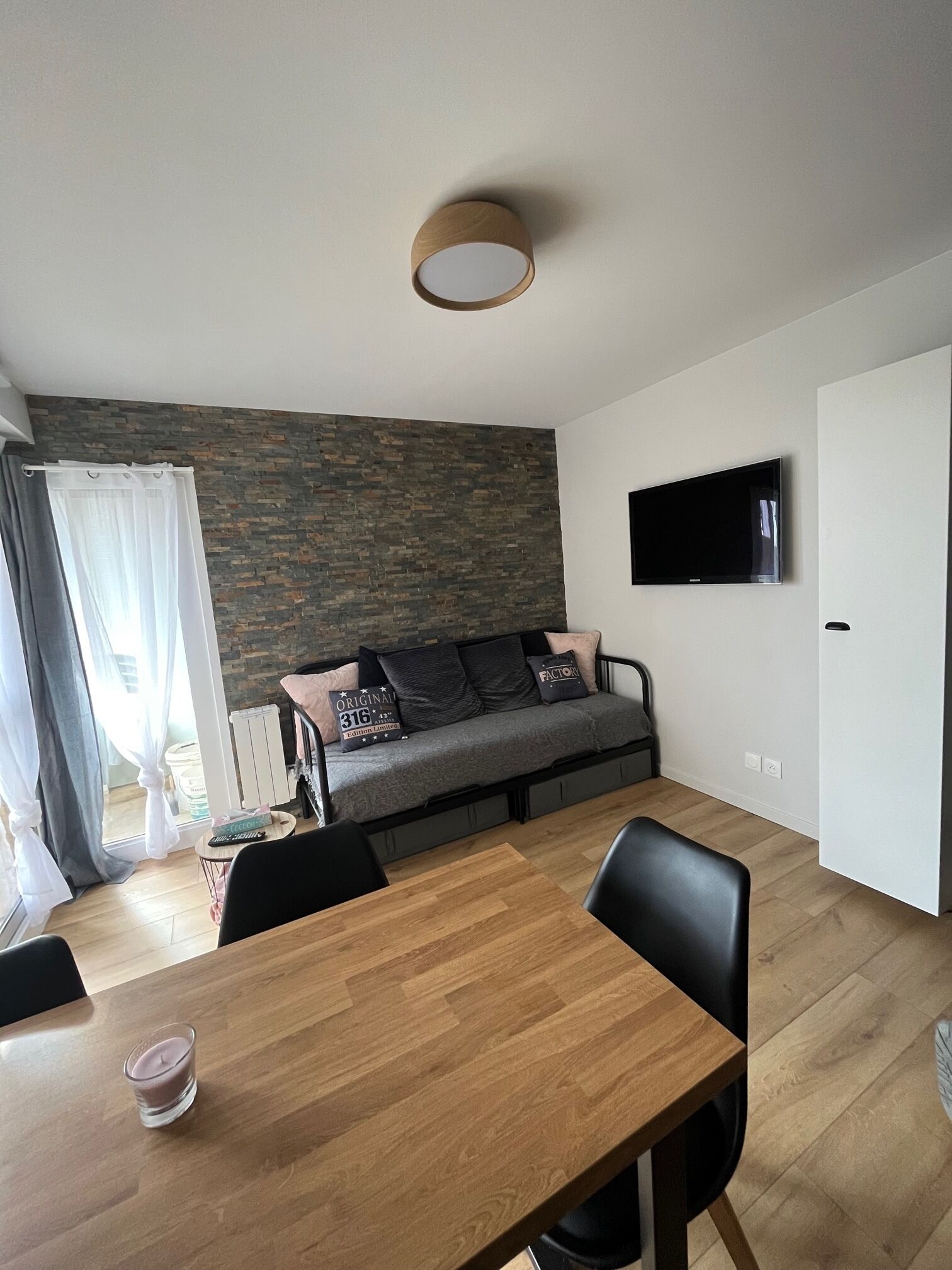 A modern living room with a sofa, a TV mounted on the wall, and a dining table with chairs.