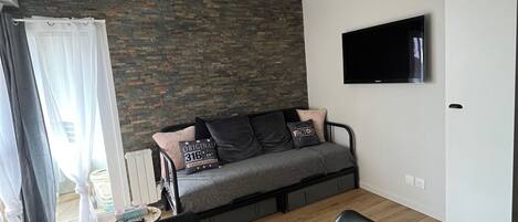 A modern living room with a sofa, a TV mounted on the wall, and a dining table with chairs.