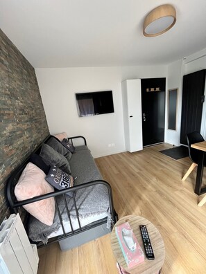 A modern living room with a grey sofa, a small round table with a remote control, and a TV mounted on the wall. - Studio in Saint Lary at the foot of the slopes (Saint-Lary-Soulan)