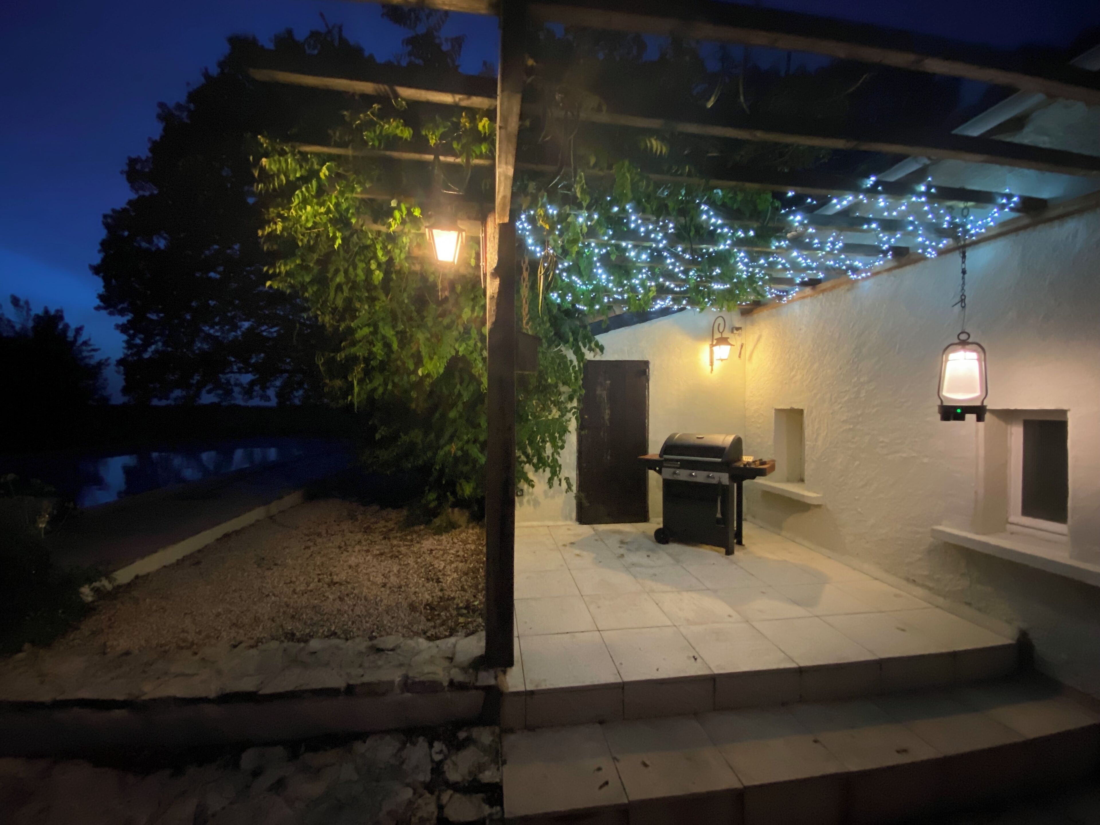 An outdoor patio area with a grill, string lights, and a pergola.