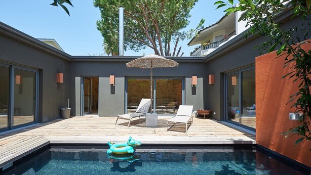 Un espace piscine extérieur moderne, doté de chaises longues, d’un parasol et d’un flotteur.