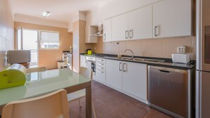 A modern kitchen with white cabinets, stainless steel appliances, and a glass dining table. - FLH Garajau Fantastic Ocean View with Balcony (Santa Cruz)