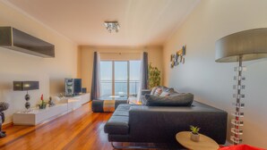 A modern living room with a sofa, TV, and a plant. - FLH Garajau Fantastic Ocean View with Balcony (Santa Cruz)