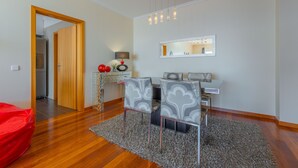 A modern living room with a wooden floor, a red bean bag, two grey patterned chairs, a small table with a lamp, and a mirror on the wall. - FLH Garajau Fantastic Ocean View with Balcony (Santa Cruz)